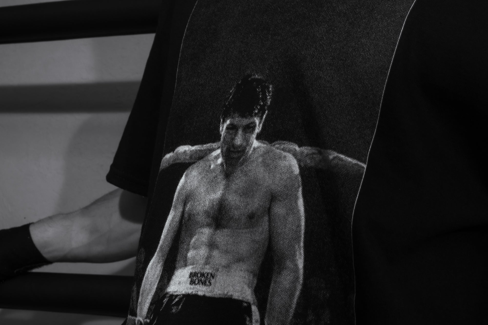 Black and white photo of a shirtless man in boxing shorts with a blurred background