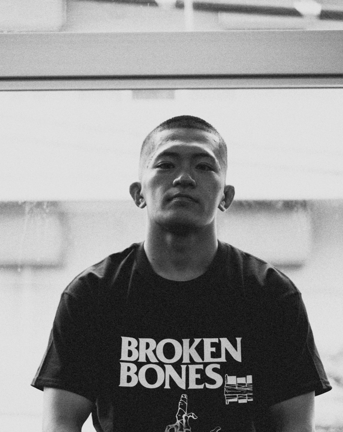 Person wearing a 'Broken Bones' t-shirt sitting on a bench.